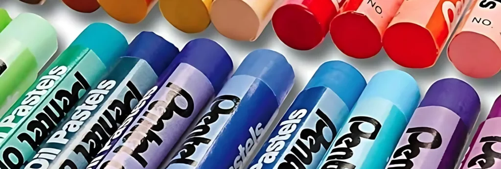 the image shows a close up of pentel oil pastels in a rainbow order and unused. they are mainly blue variations in the front. the background ones are slightly out of focus. 