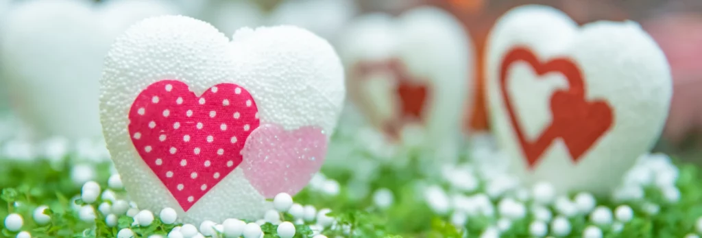 the image is showing a few hearts made of polystyrene. sitting on green grass. the hearts have fabric on them that is pink with white polka dots and red cut out hearts. 3 hearts are visable and there is polystyrene balls on the grass.