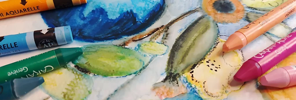 the image is a close up of the neo colour pastels that have been used to draw pictures of fruit on paper which is beneath them. the colours are in shades of orange, green, blue and pinks