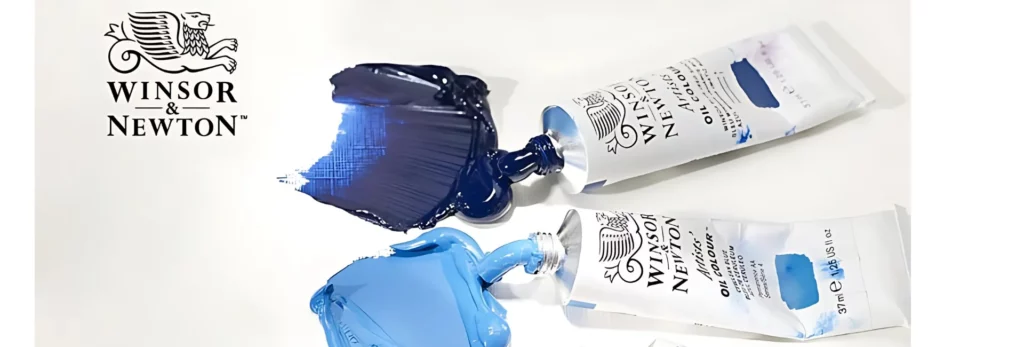 in the center of the image are two tubes of different shades of blue oil paint, their caps are off and the two different blues have been squeezed out onto the surface. and smeared down in sections with a palette knife. the top left hand side there is the black and white winsor and newton logo of a lion and the name. on a white background